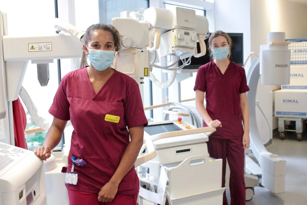 Two nurses in scrubs in hospital pictured with equipment