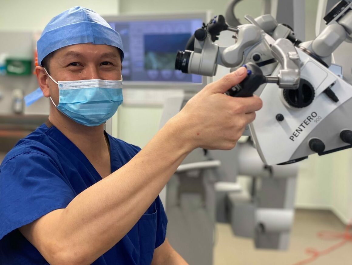 Neuro surgeon Mario Teo sits in an operating theatre in blue scrubs and a mask.