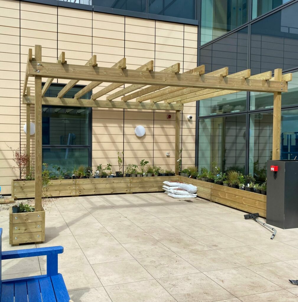 A picture of a wooden canopy, surrounded by planters in the new garden