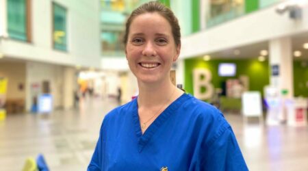Dr Rachel Scott, co-founder of Bleep101, is wearing blue scrubs and standing in Southmead Hospital's Brunel Building