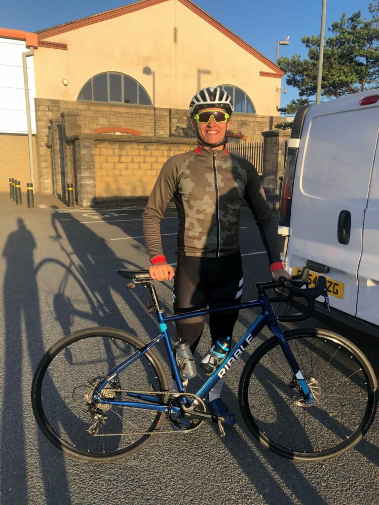 Josh stands behind his bike in exercise gear