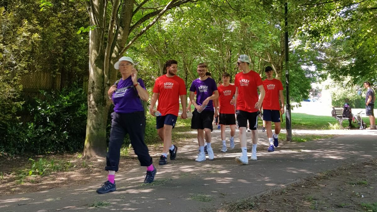 Group of people in red and purple Southmead Hospital Charity t-shirts walking through a wooded area.